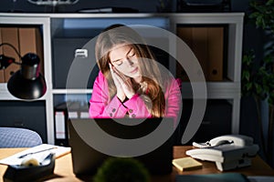Young caucasian woman working at the office at night sleeping tired dreaming and posing with hands together while smiling with