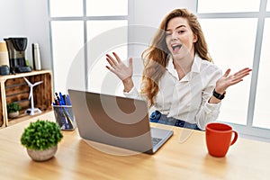 Young caucasian woman working at the office using computer laptop celebrating crazy and amazed for success with arms raised and