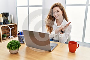 Young caucasian woman working at the office using computer laptop clapping and applauding happy and joyful, smiling proud hands