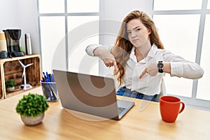 Young caucasian woman working at the office using computer laptop pointing down looking sad and upset, indicating direction with