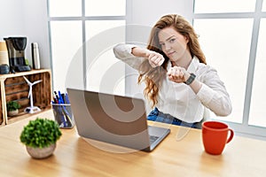 Young caucasian woman working at the office using computer laptop punching fist to fight, aggressive and angry attack, threat and