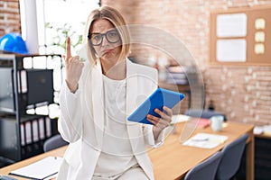 Young caucasian woman working at the office wearing glasses pointing up looking sad and upset, indicating direction with fingers,