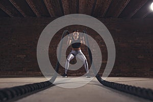 Young caucasian woman working out with battle ropes at a gym
