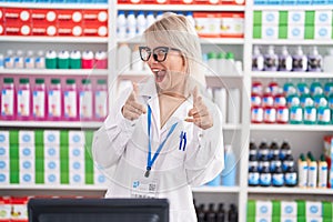 Young caucasian woman working at pharmacy drugstore pointing fingers to camera with happy and funny face