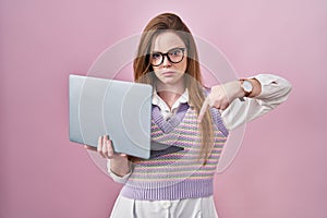 Young caucasian woman working using computer laptop pointing down looking sad and upset, indicating direction with fingers,