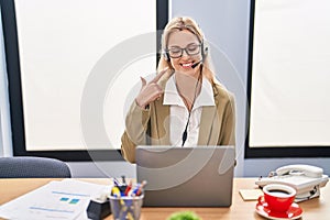 Young caucasian woman working wearing call center agent headset smiling happy pointing with hand and finger