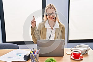 Young caucasian woman working wearing call center agent headset smiling happy pointing with hand and finger to the side