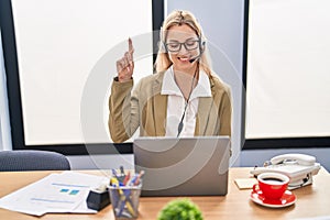 Young caucasian woman working wearing call center agent headset smiling with an idea or question pointing finger with happy face,