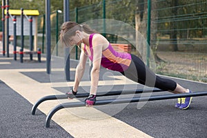 Young caucasian woman workouts on the park sports ground. The girl in a sports plank position, in black and lilac sportswear. Whit