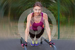 Young caucasian woman workouts on the park sports ground, in a plank position, bright sportswear.