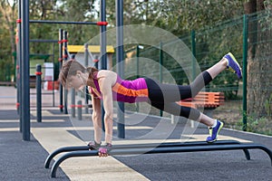 Young caucasian woman workouts on the park sports ground. In a sports plank position, bright sportswear.