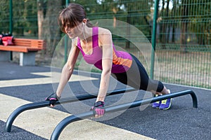 Young caucasian woman workouts on the park sports ground. In a sports plank position, bright sportswear.