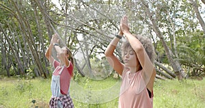 Young Caucasian woman and young biracial woman practice yoga outdoors