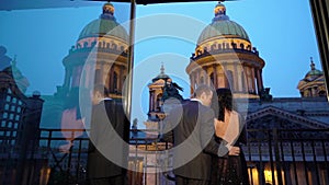 Young caucasican man in suit and brunette woman in black luxury dress staying at balcony in a city