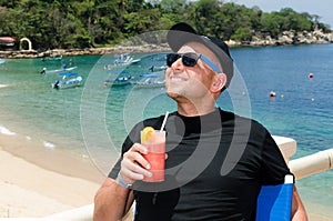 Young caucausian man enjoys coctail at ocean resort during summ