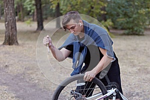 Young causacian man with screwdriver tries to damage the bicycle wire at the abandoned park. Vandal actions.