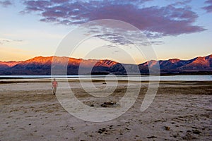 Young causacian man walking on beach at beautiful Lake Tekapo with mountain range in the Background on sunset with clouds, South