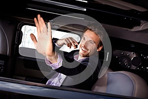 Young celebrity waving from limousine smiling