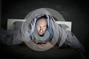 Young cell phone addict man awake late at night in bed using smartphone