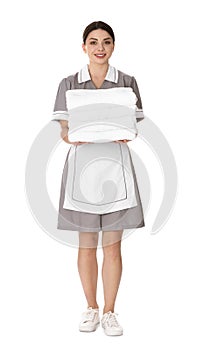 Young chambermaid holding stack of fresh towels on background