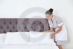 Young chambermaid making bed