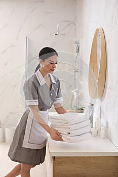 Young chambermaid putting stack of towels on countertop in bathroom