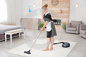 Young chambermaid removing dirt from carpet with vacuum cleaner