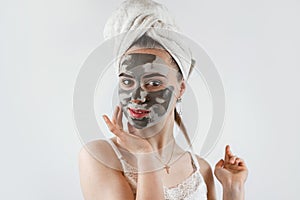 Young charm woman wear towel pampering face with mud or black clay facial mask  on grey