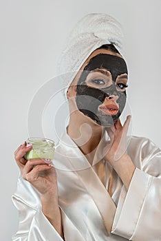 Young charm woman wear towel pampering face with mud or black clay facial mask  on grey