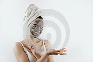Young charm woman wear towel pampering face with mud or black clay facial mask isolated on grey