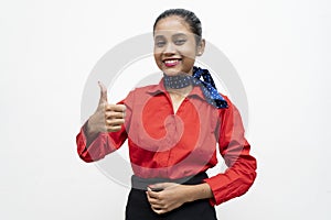 Young charming air hostess in red uniform showing thumbs up in the camera with a smile on her face