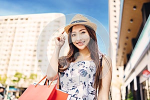 Young charming asian woman holding shopping bags on the street