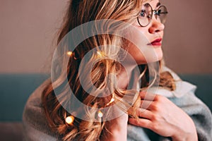 Young charming blonde woman in glasses with lights in her hair, romantic atmospheric photo about dreams