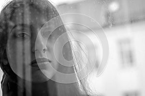 Young charming brunette girl behind a glass window