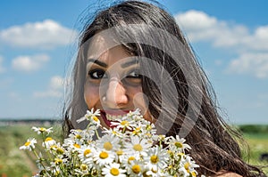 Young charming brunette girl with a bouquet of white field chamomiles on a summer sunny day