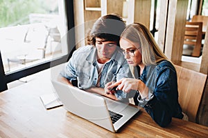 Young charming couple using laptop while sitting at cafe