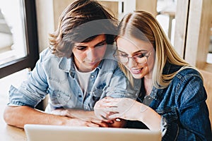 Young charming couple using laptop while sitting at cafe