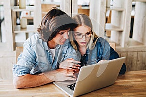 Young charming couple using laptop while sitting at cafe