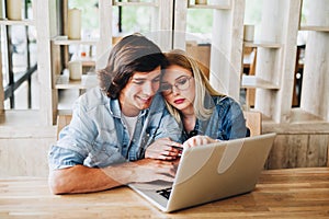 Young charming couple using laptop while sitting at cafe