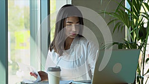 Young charming female freelancer using laptop computer for distance job while sitting in modern coffee shop interior
