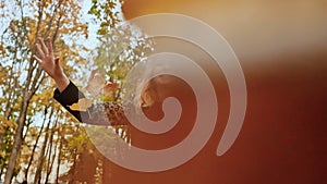 Young charming girl in a coat throws colorful autumn leaves, posing and laughing in the camera. Enjoying the autumn