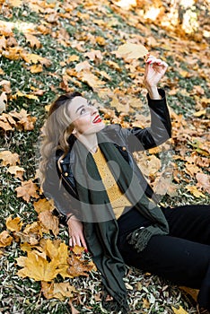Young charming girl with curled long blonde hair and red lipstick on her lips is enjoying autumn