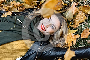 Young charming girl with curled long blonde hair and red lipstick on her lips is enjoying autumn