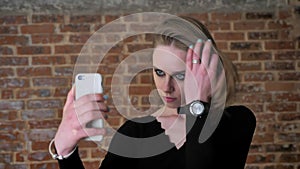 Young charming girl with smoky eyes make seifie on her smartphone, communication concept, brick background