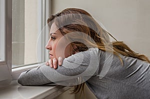 Young charming girl student, with long hair, sad at the window reading book with lessons