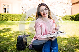 Young, charming girl student reads book against background of green grass and blossom tree