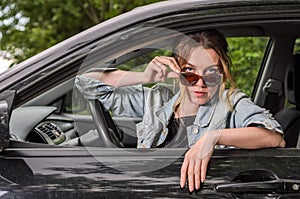 Young charming girl in sunglasses is sitting at the wheel of a car