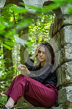 Young charming girl the teenager with long hair sitting on the sad ruins of an ancient stone castle window in Striysky Park in Lvi