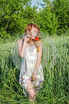 Young charming girl in a white sundress beautiful, walking in the field among the wheat spikelets with flower red poppies in