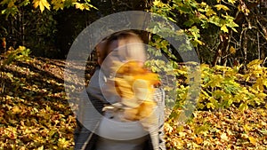 Young charming mother whirls holding her baby daughter in her arms among yellow fallen maple leaves, happy family